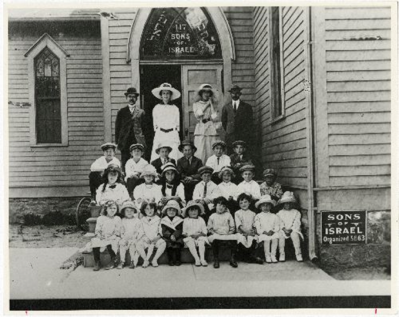 Black and white photo of adults and children in front of school.