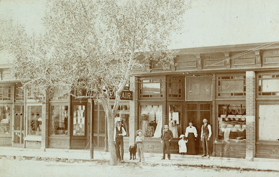 Black and white photo of people in front of a storefront. (Circa 1890).