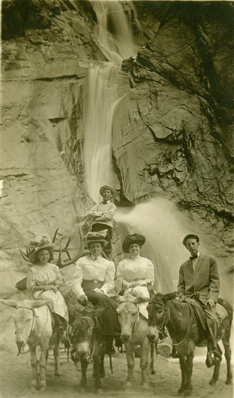 Black and white photo of three women and a man on burros.