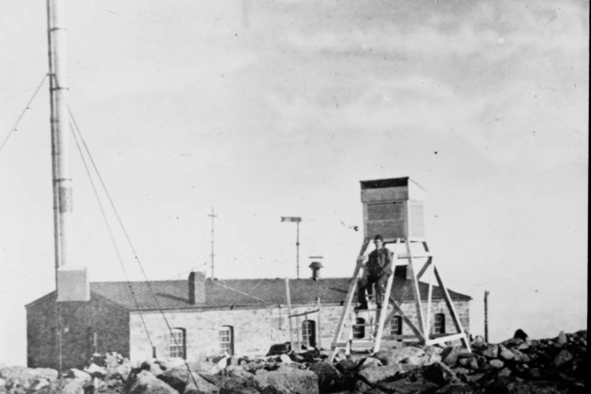 Black and white photo of a weather tower on a mountain.