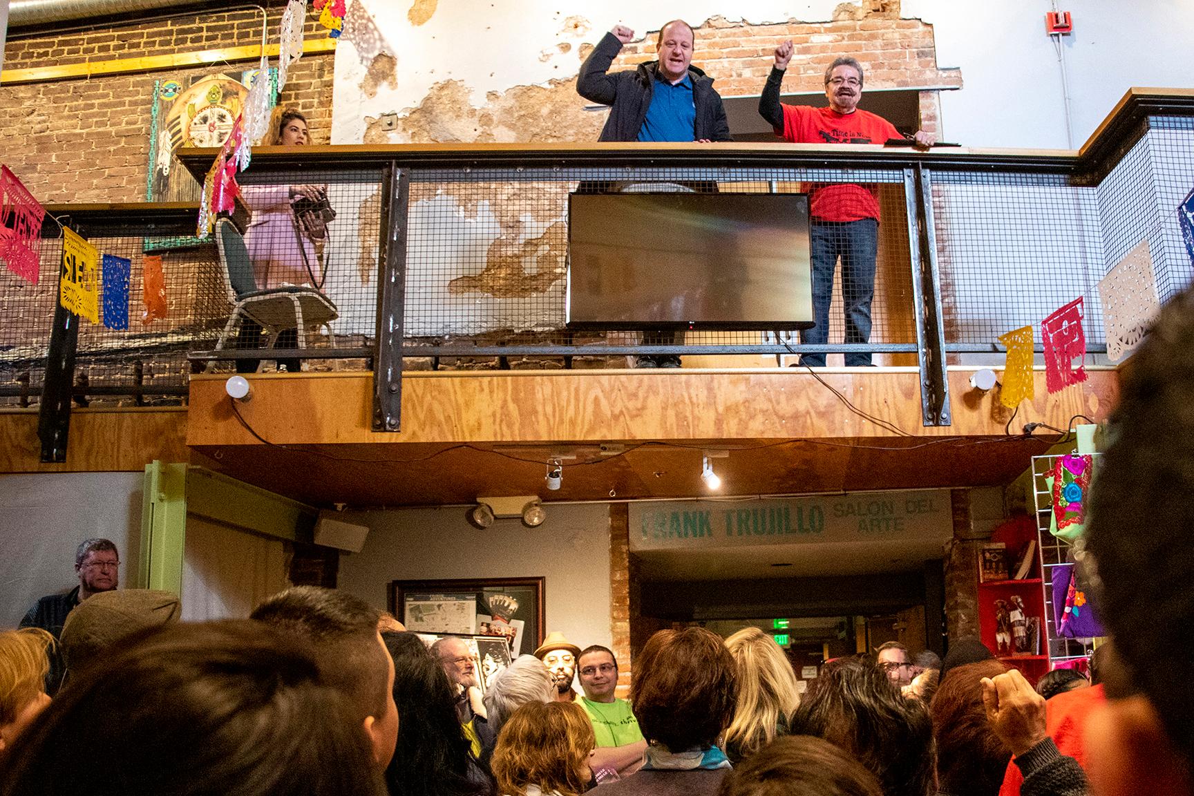 Gov. Jared Polis (left) raises a fist alongside Ramon Del Castillo