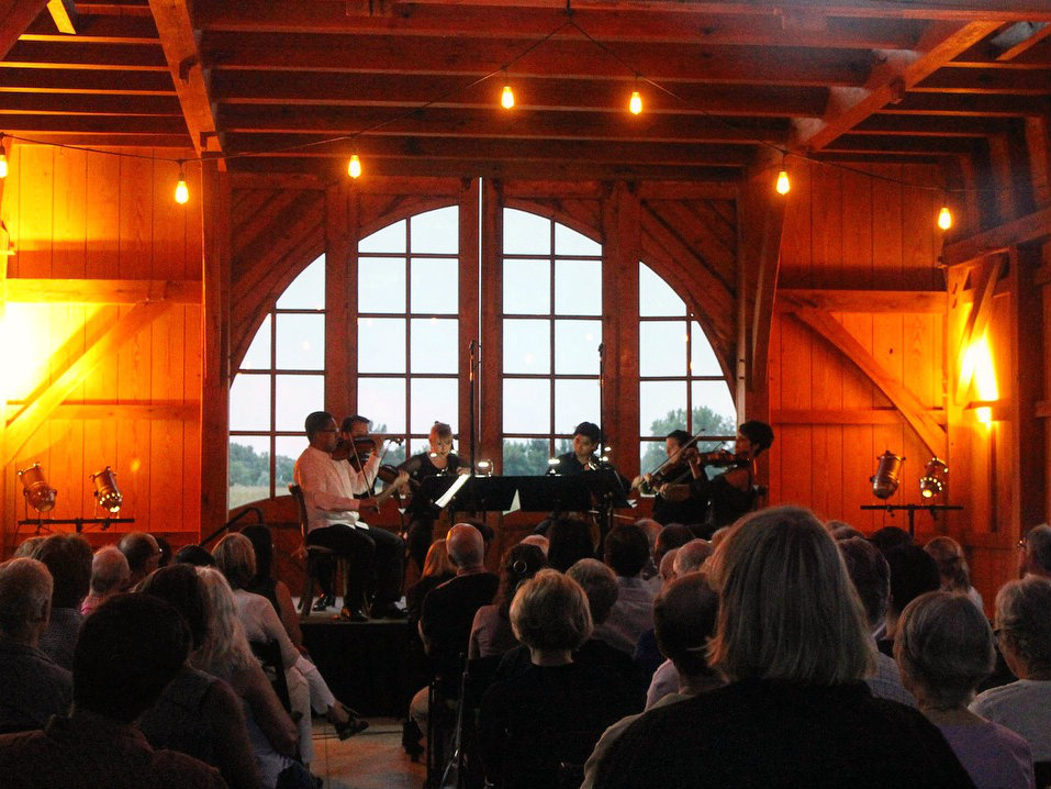 A string sextet performing in front of an audience in a dimly lit hall in Boulder, Colorado.