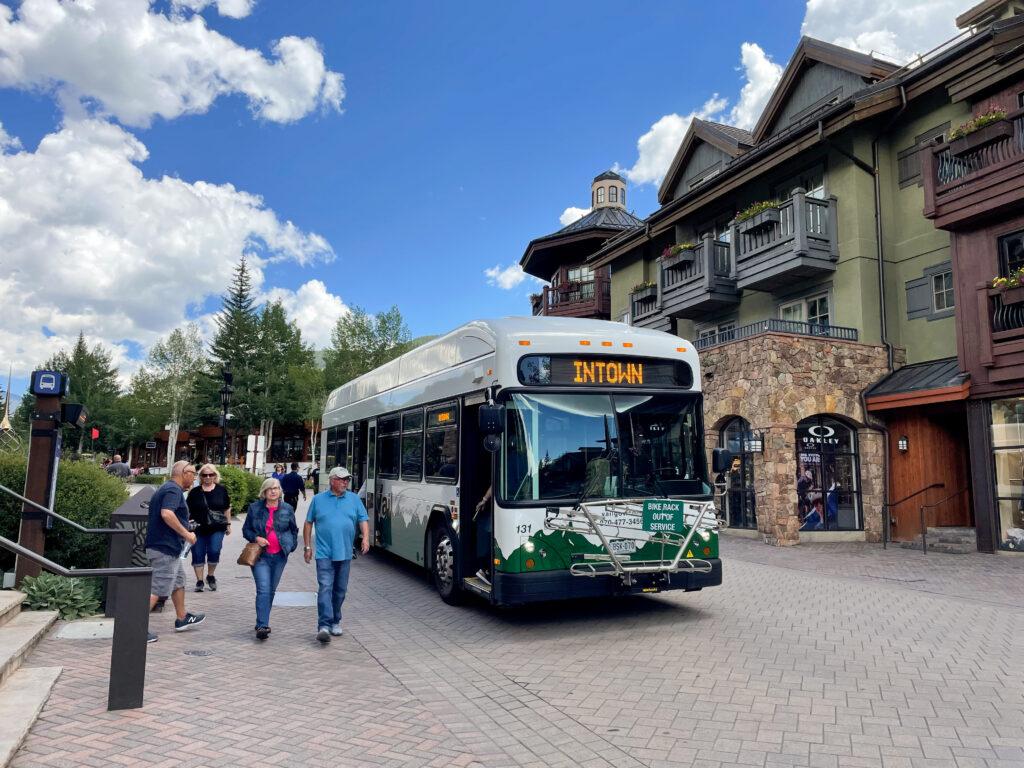 A group of people get off an electric bus in vail with condos in the background.