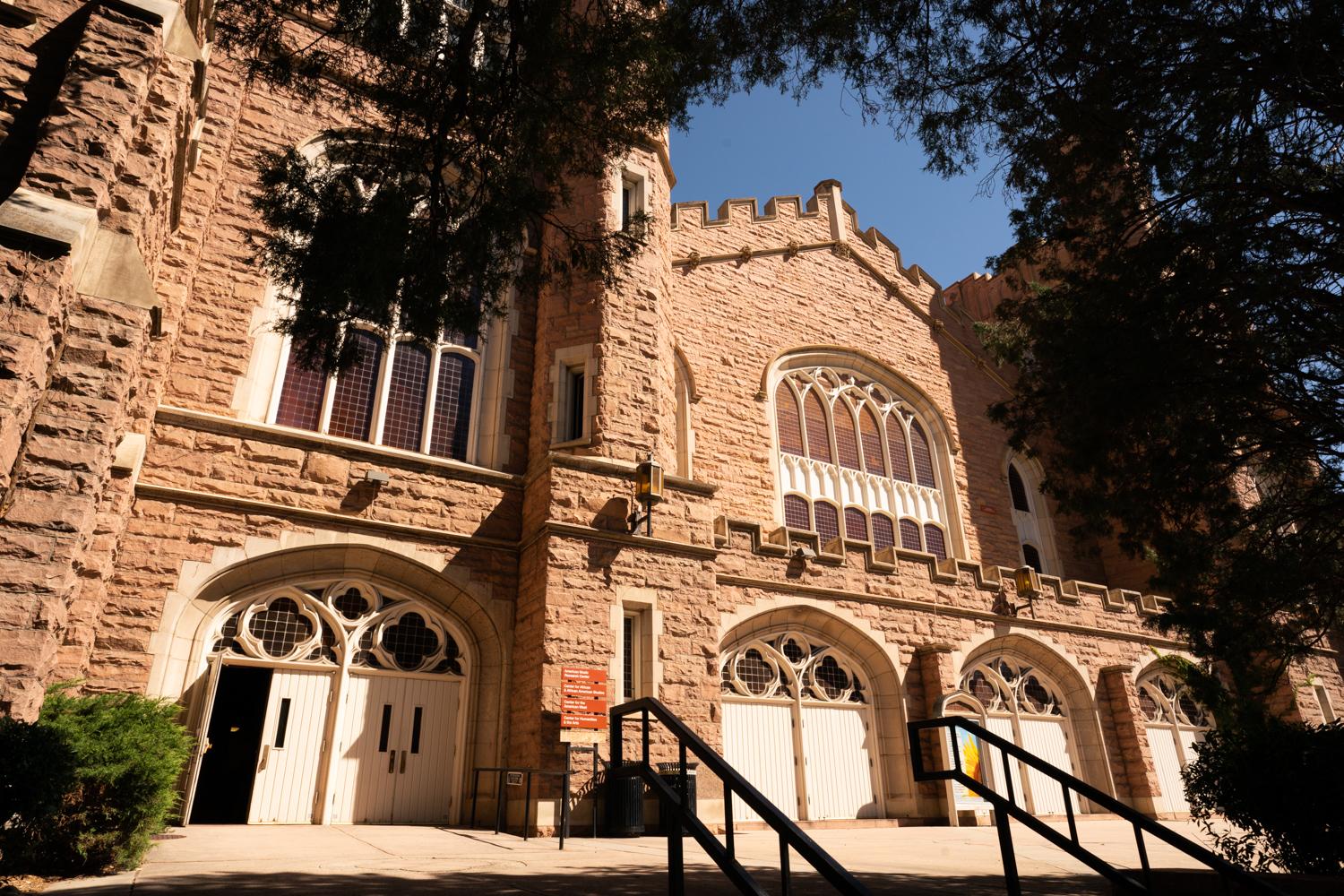 A large stone building is framed by a large tree in Boulder, Colorado, under a sunny sky.