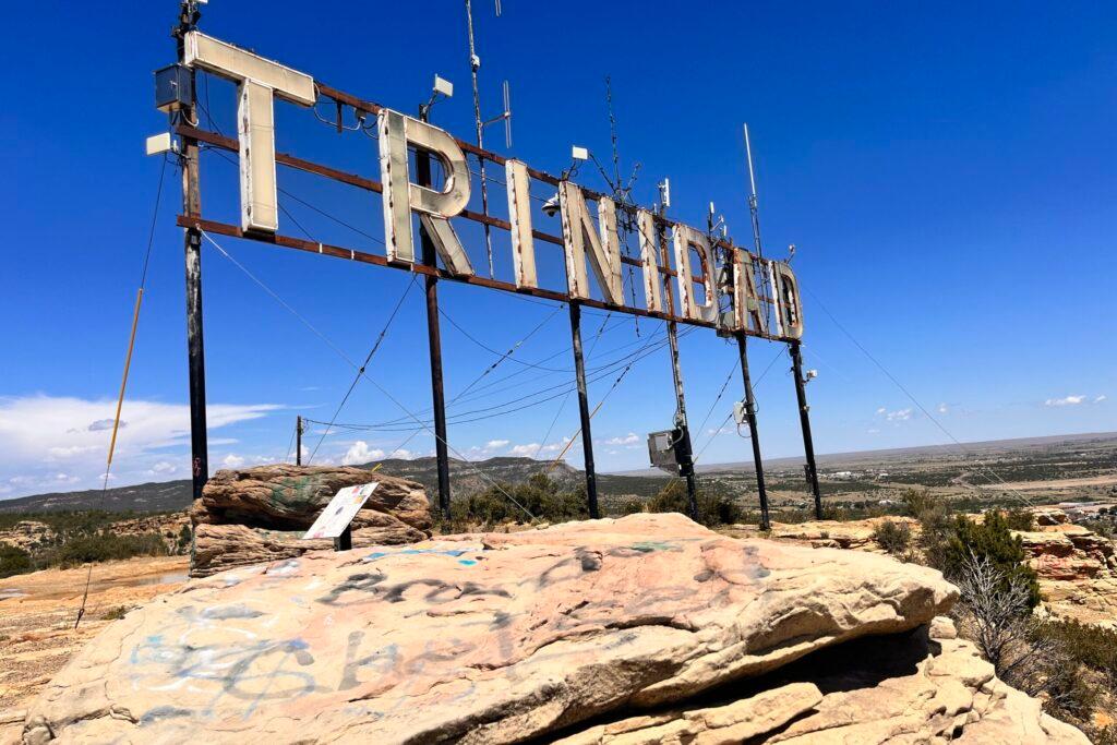 A shutoff neon sign that says Trinidad on top of a small mountain on a bright day.