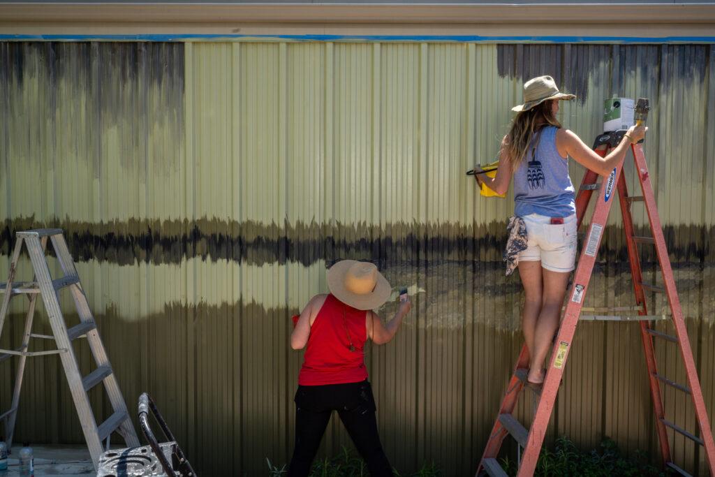 TWO FEMALE MURALISTS PAINTING A SCENE ON A WALL