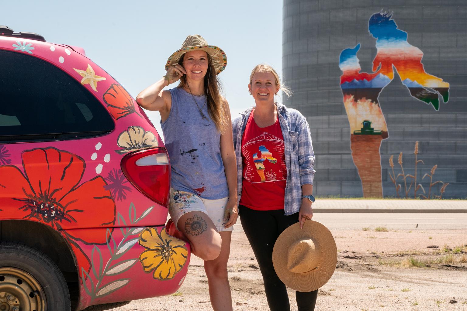 TWO WOMEN ARTISTS STAND NEAR THEIR FARMER MURAL