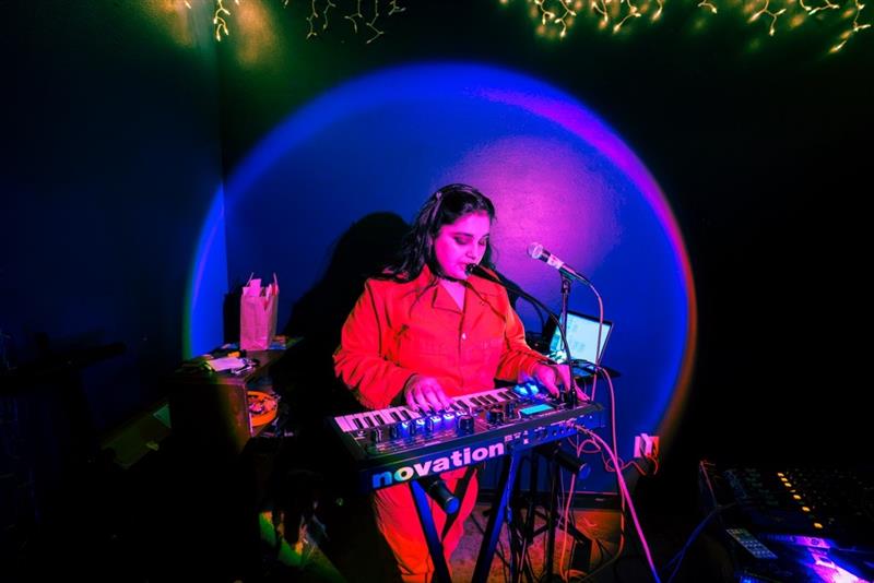 Photo is of Vidushi Goyal, lead vocalist and synth player of Mr. Knobs during a live performance.