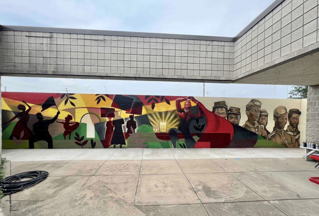 A mural for Juneteenth made up of multiple illustrations of people and soldiers to the right side covered by a black green and red flag.