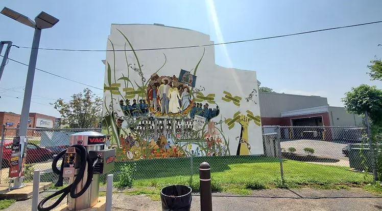 A mural on the side of the wall celebrating Juneteenth with a group of people in the middle, broken green chains and a white background.
