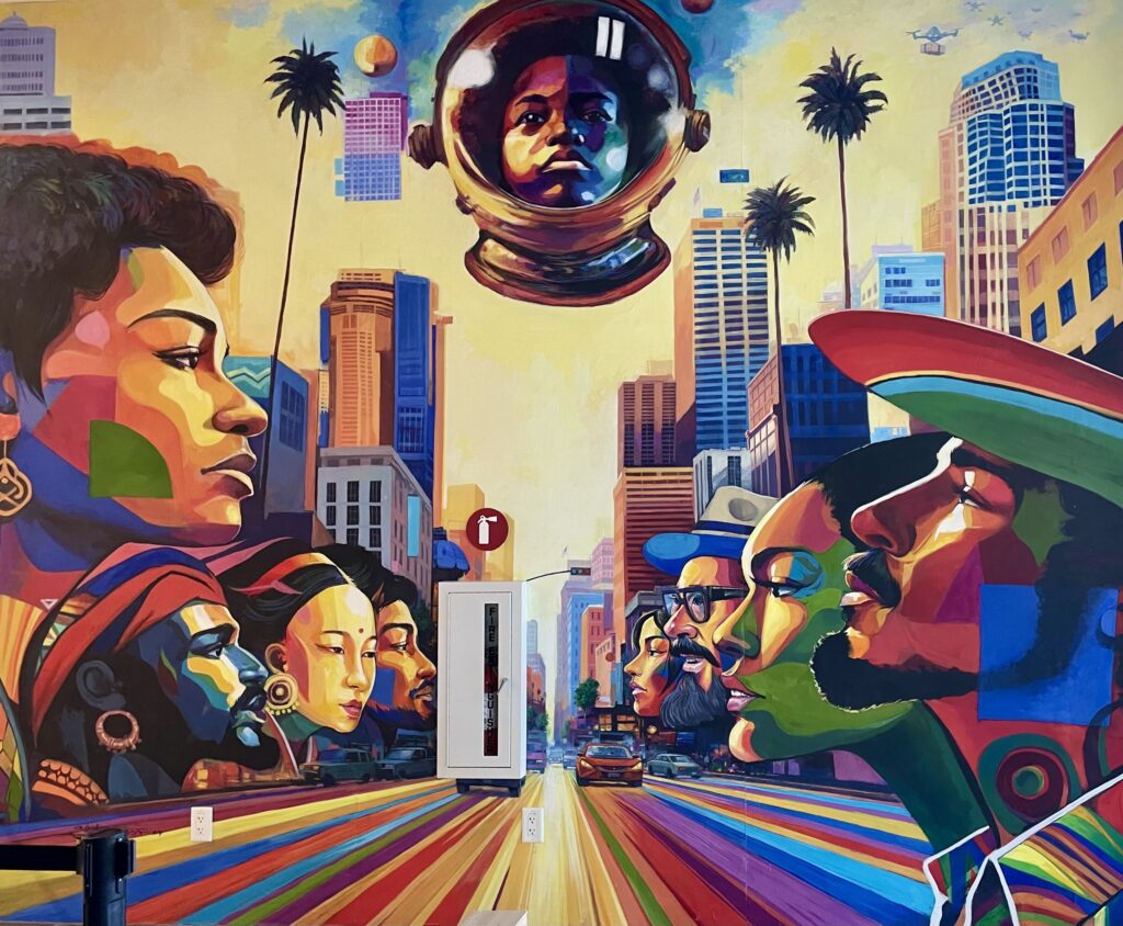 A mural depicting people's faces along both sides of a road facing inward in multicolored paint as a cityscape looms above.