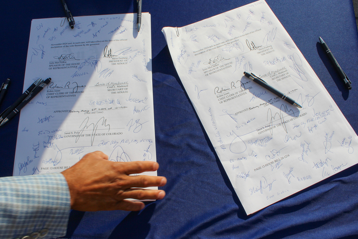 Two pieces of paper with many signatures on them sit on a table with a blue tablecloth.