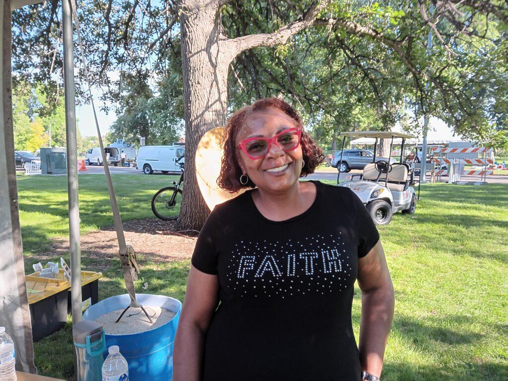 A woman in glasses and a black T-shirt stands near a tent.