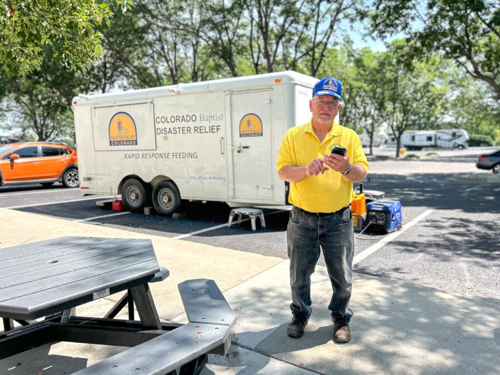 A volunteer on his cell phone in front of a trailer at a wildfire evacuation center.