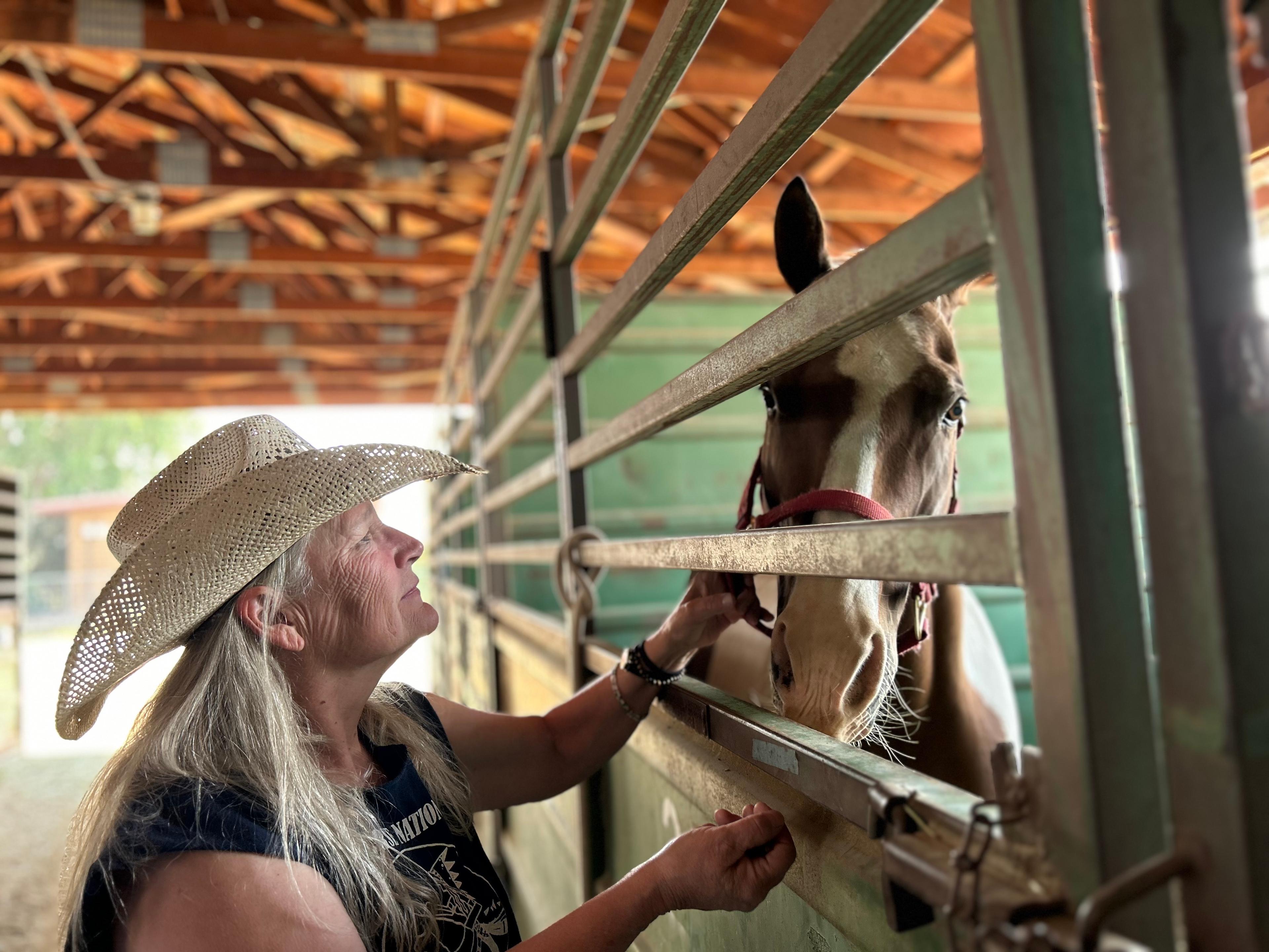 A woman in a cowboy hat sooths a horse in a barn after evacuating a wildfire.