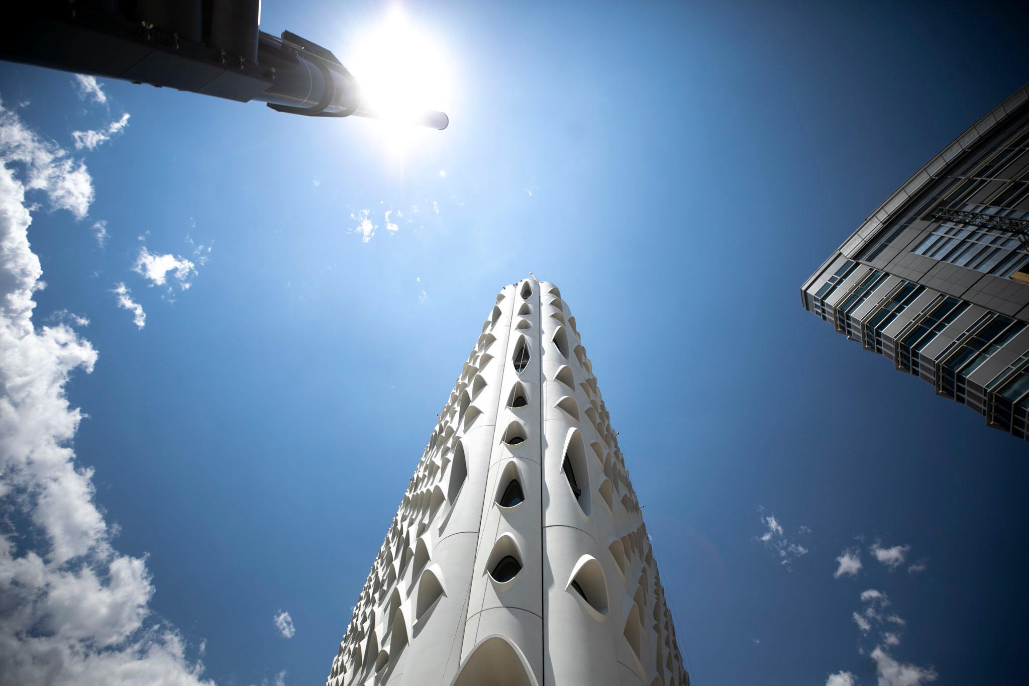 An acute white building stretches into a blue sky; it's covered with eyeball-shaped openings.