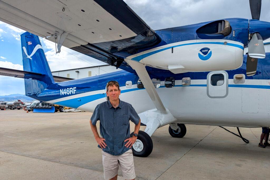 Steven Brown stands in front of an airplane that's blue and white.