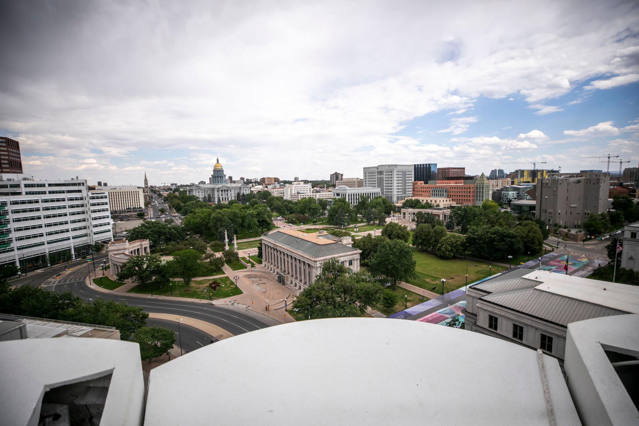 The Colorado Capitol's gold dome stands over a green park, punctuated by stone buildings. The city rises around the edges.