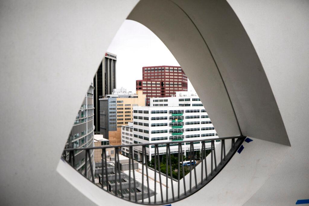 An eyeball-shaped window through a concrete wall reveals skyscrapers colored in white, yellow, blue, red and black.