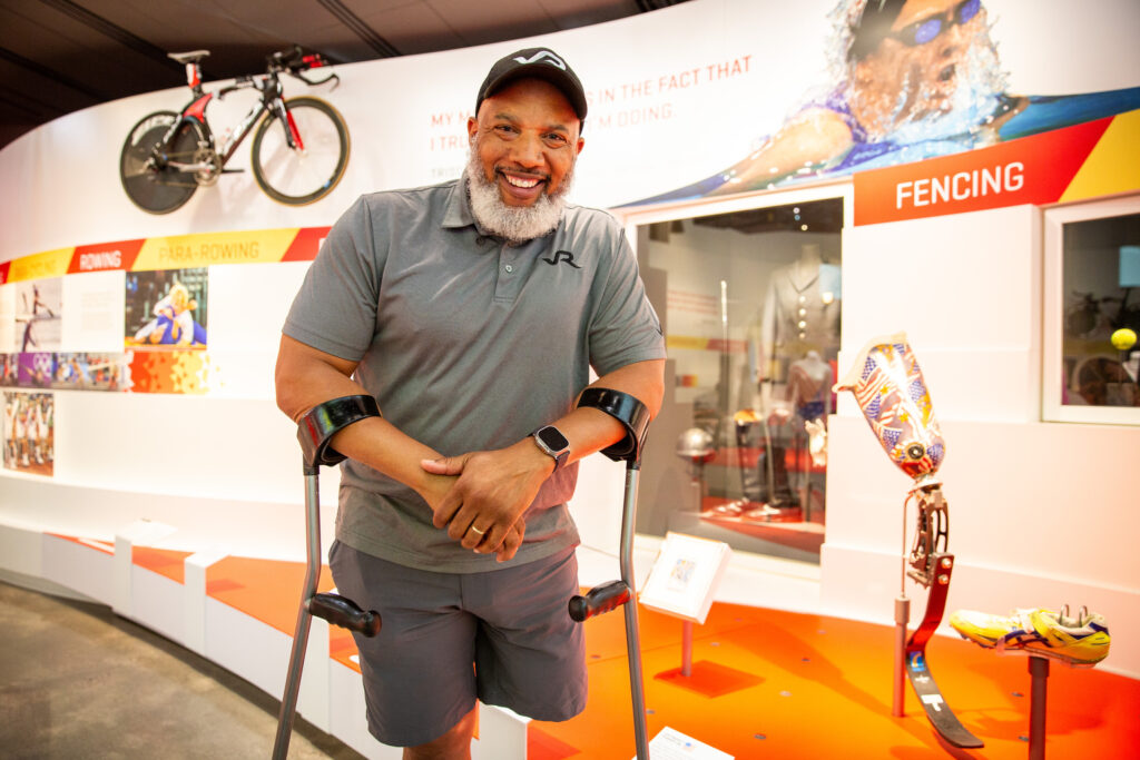 John Register poses near the display of his prosthetic leg and track shoe.