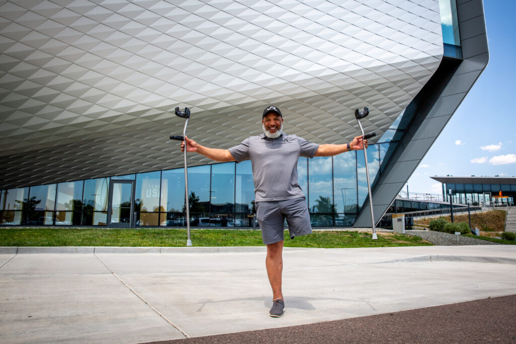 John Register stands on one leg with arms outstretched in front of the U.S. Olympic and Paralympic Museum.