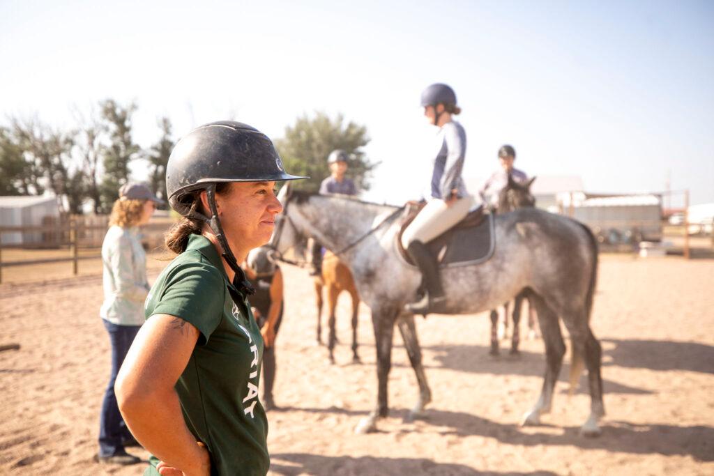 A woman in a riding helmet looks proudly out of frame; people on horseback sit behind her.