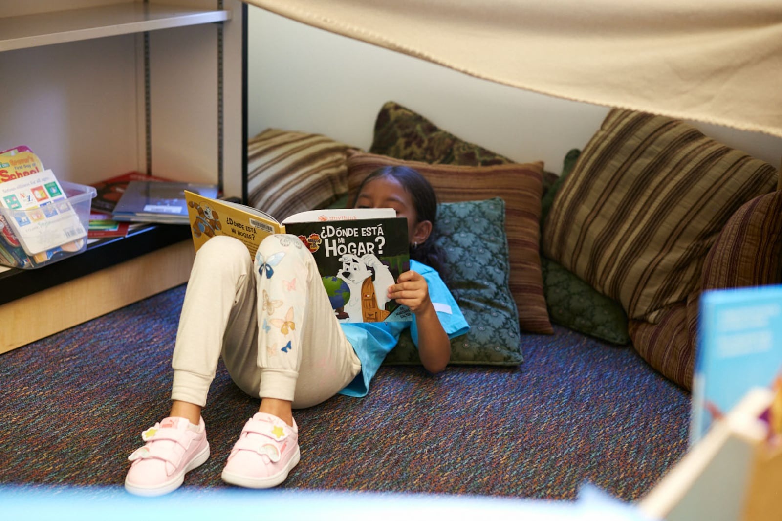 A girl lays down on the floor against pillows reading a book.