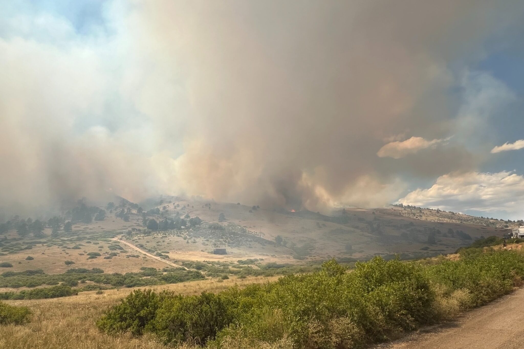 Smoke from the Stone Canyon Fire is visible in the distance in a hilly area.