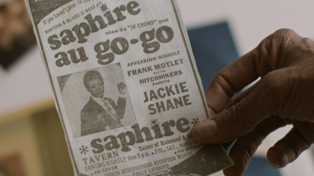 A hand holds a flyer with the inscription “Saphire au go-go” and advertises Jackie Shane