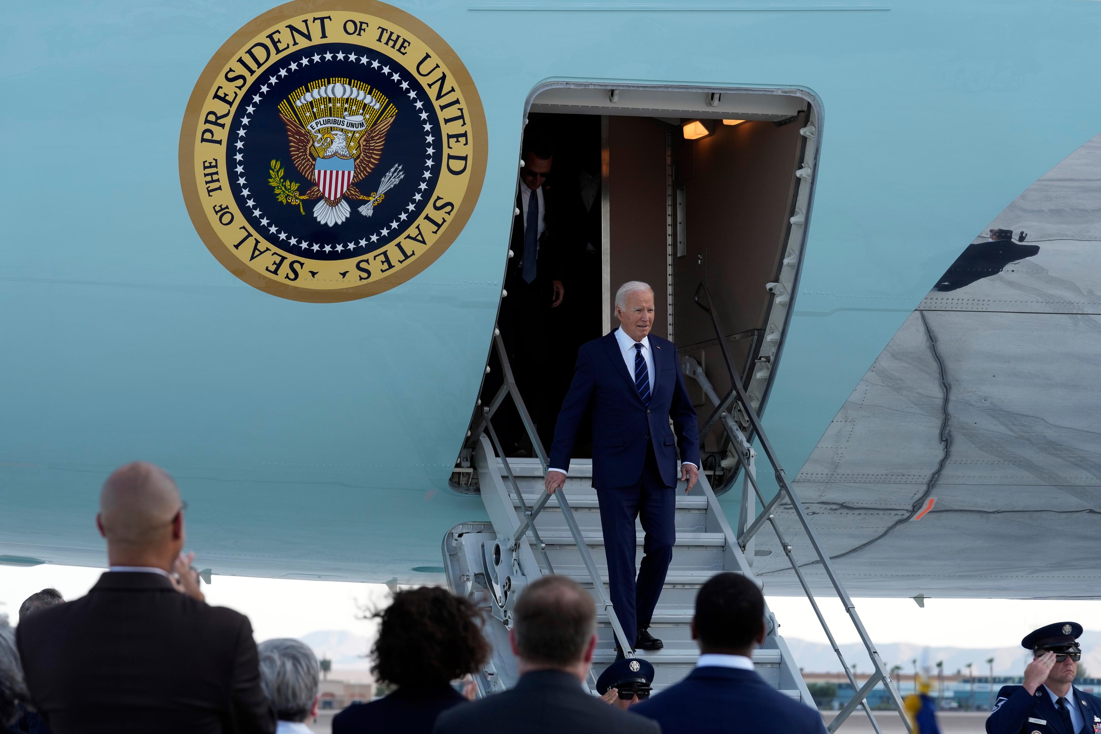 President Joe Biden walks down a flight of stairs out of an airplane while people watch.