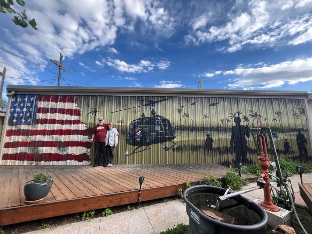 Everett Churchwell has his arm around his wife Norma as they stand in front of a mural in Limon depicting his Army helicopter service in Vietnam.