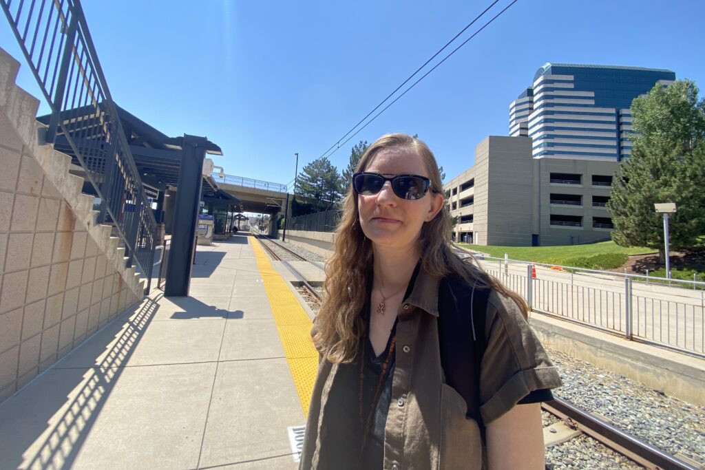 A woman stands at an RTD station by the track.