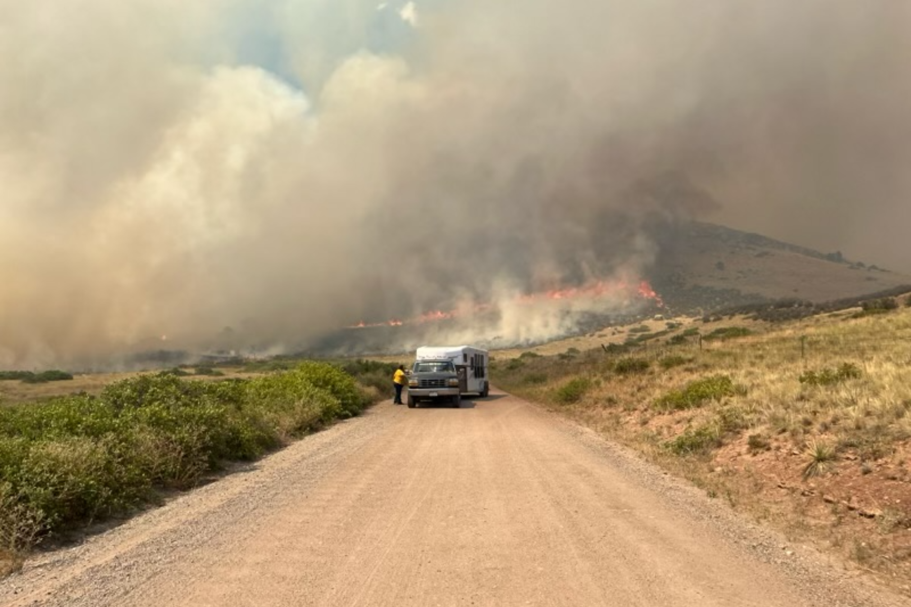 Smoke billows from the Stone Canyon fire along a dirt road with flames visible in the background.