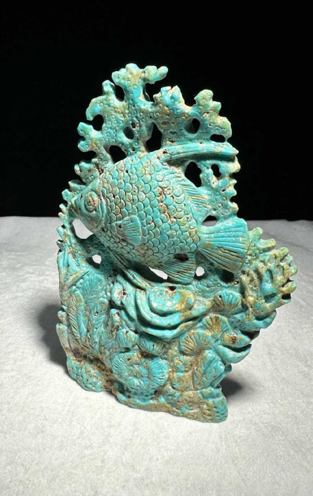 Light green-ish blue turquoise with gold spots carved into the shape of a fish and a coral reef