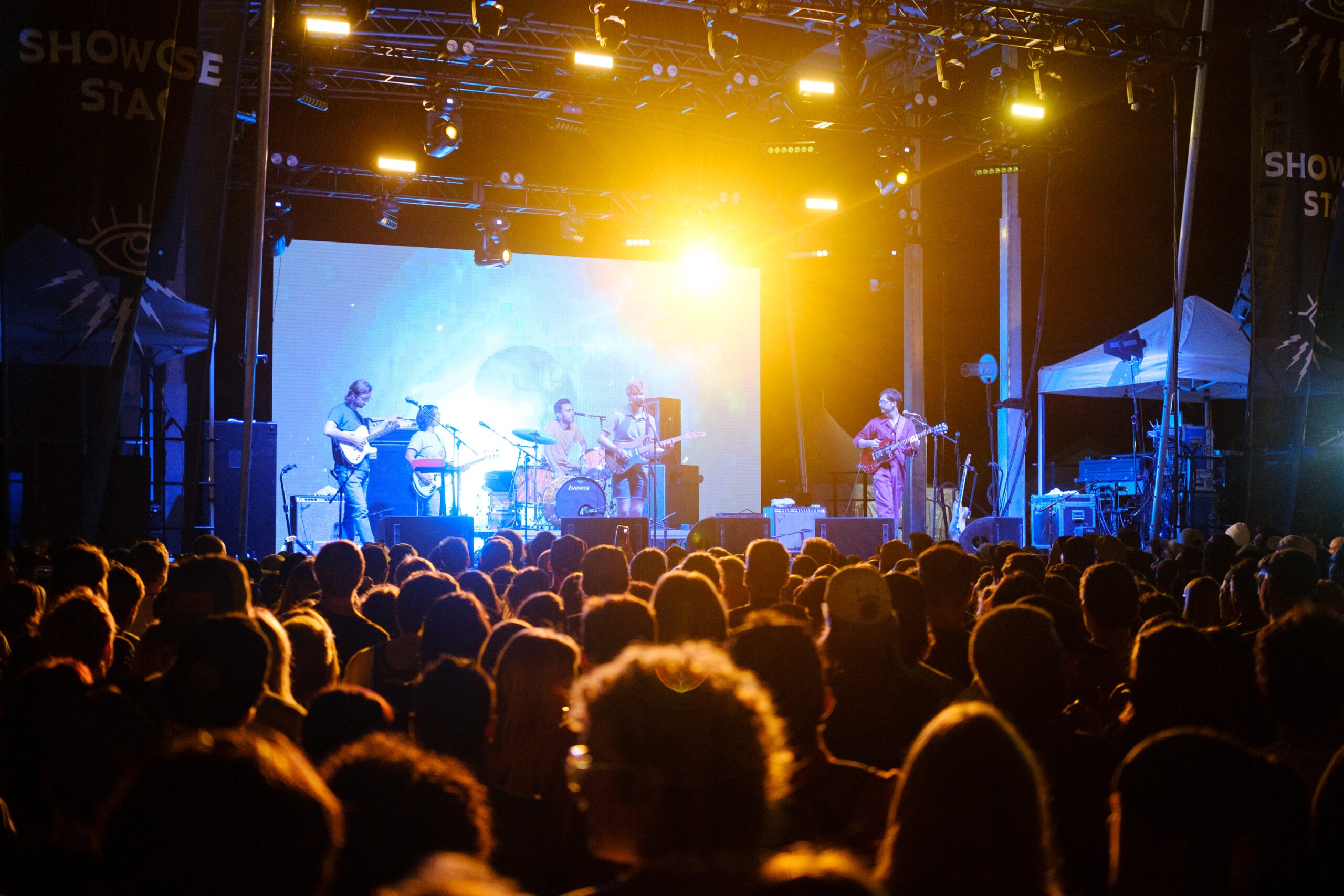 A crowd of people looking toward a stage where a band performs in dim lighting.