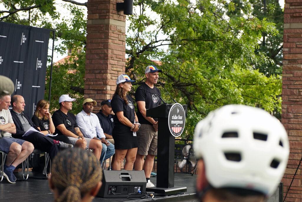 A woman and a man stand at a podium with a "Ride for Magnus" sign it.