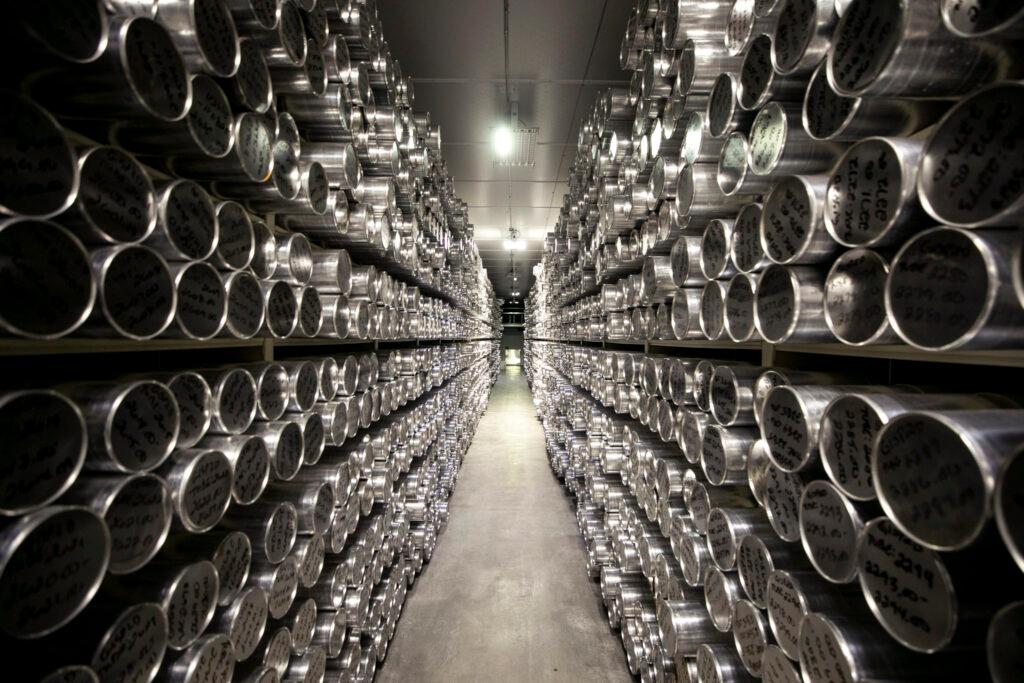 A long hallway stretches between rows of shelves, each totally filled with tubes; their metal lids shine all the way down the line.