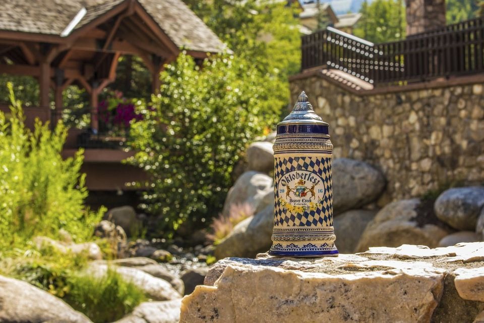 A Beaver Creek Oktoberfest stein posed creek side with greenery and a path in the background.