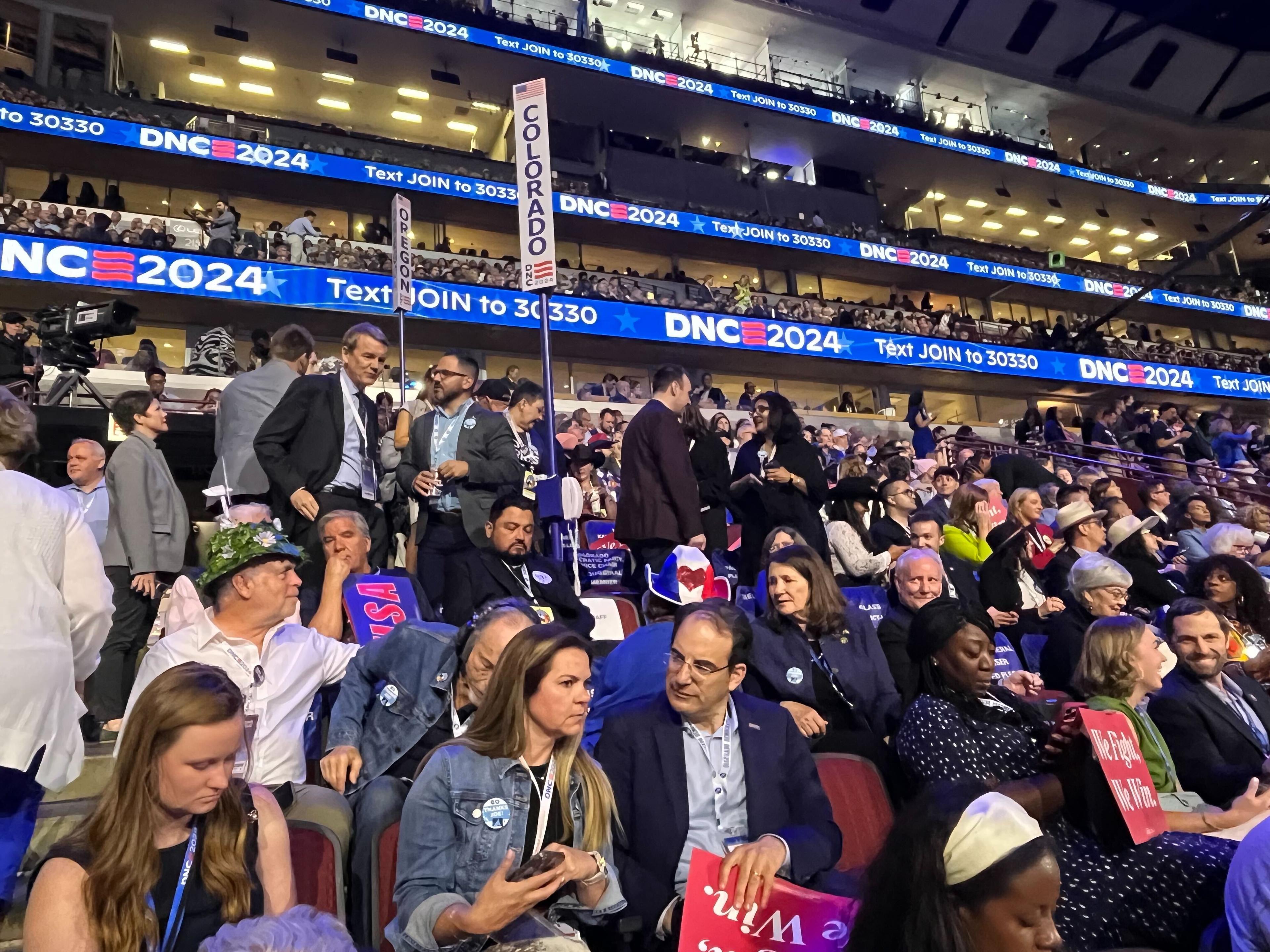 A crowd of delegates, including Attorney General Phil Weiser, Senator Michael Bennet and Reps Diana DeGette and Jason Crow sit in the audience at the Democratic National Convention.