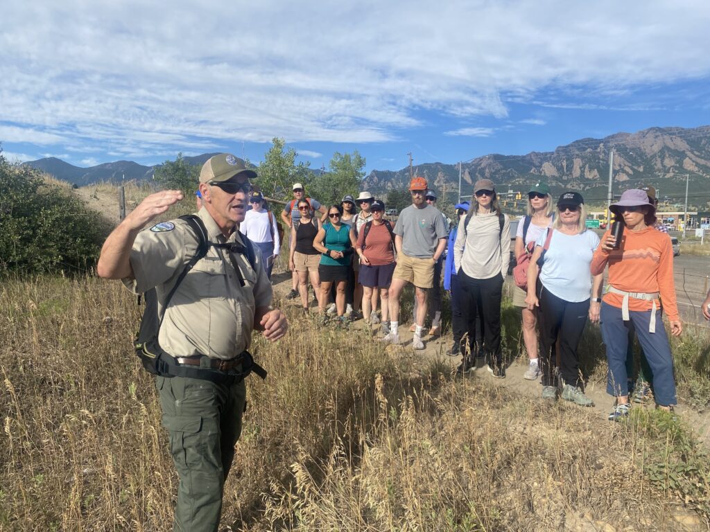 A park ranger gestures in an open space as a line of climate medicine students listens.