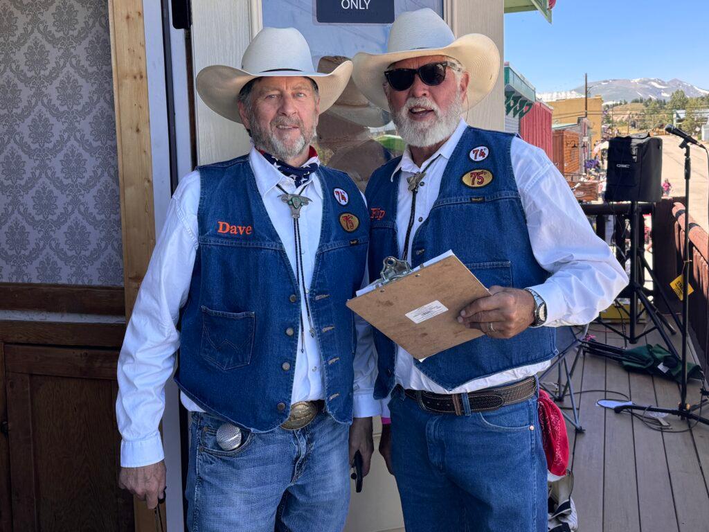 Two men in denim and cowboy hats stand on a balcony facing the camera.