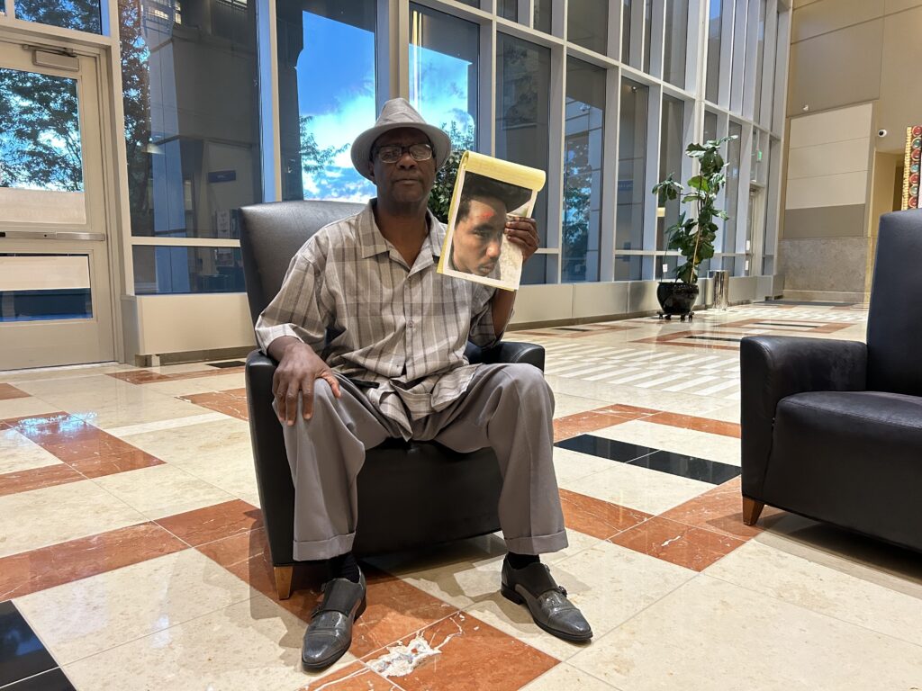 A man in Aurora City Hall lobby holds photo of his godson.