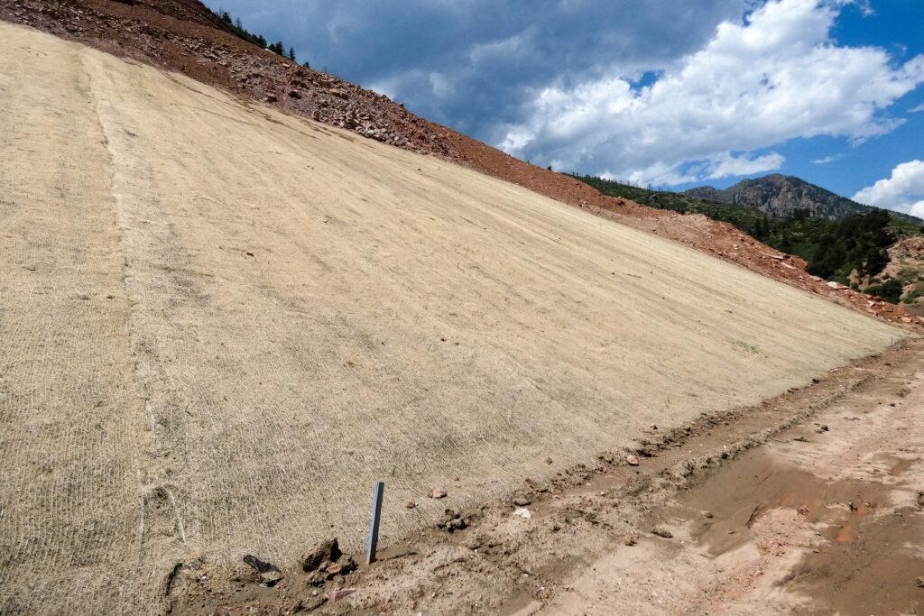 Straw-colored net covers red-colored soil on a steep slope