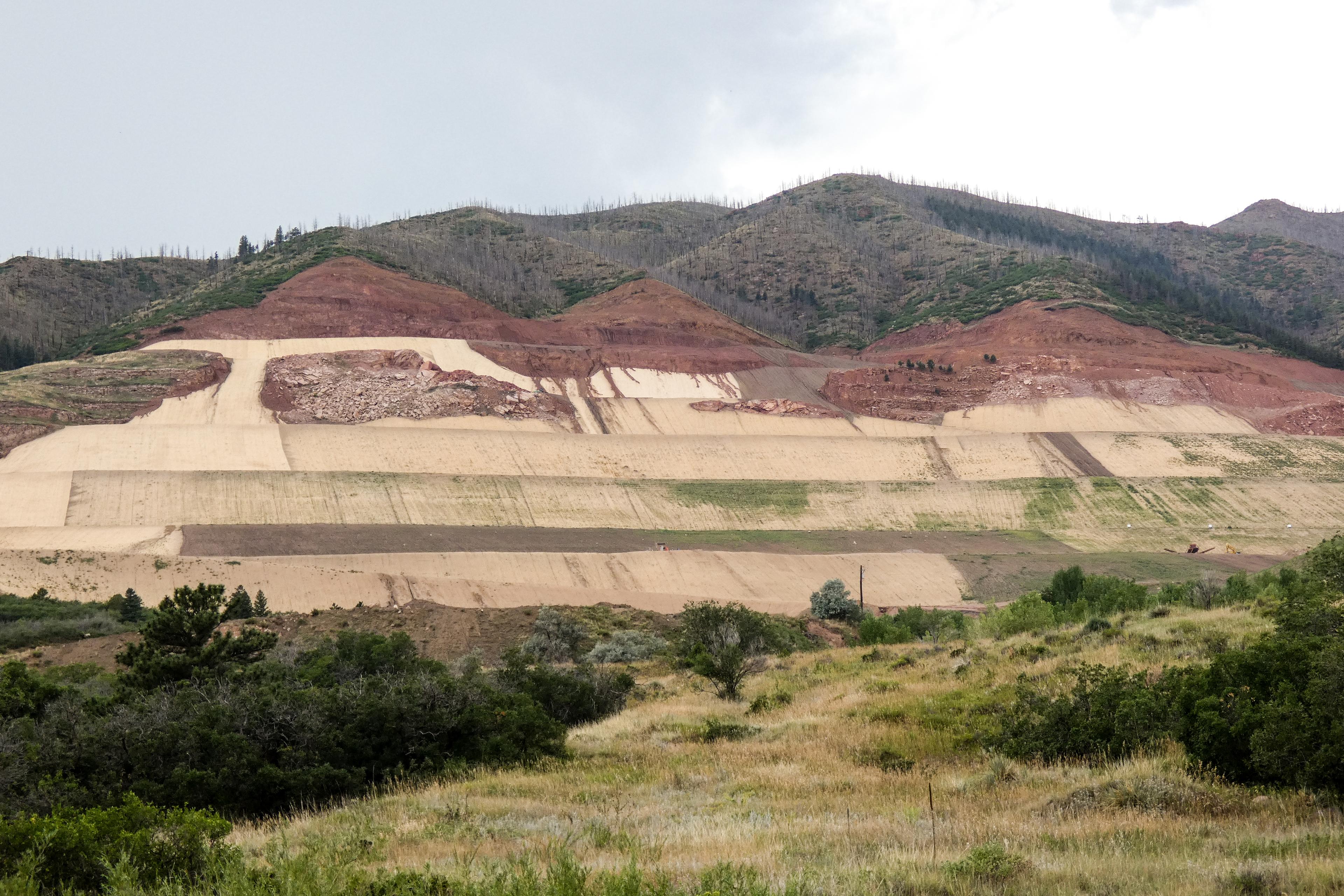 Several large terraces carved into a hillside are covered with straw colored netting.