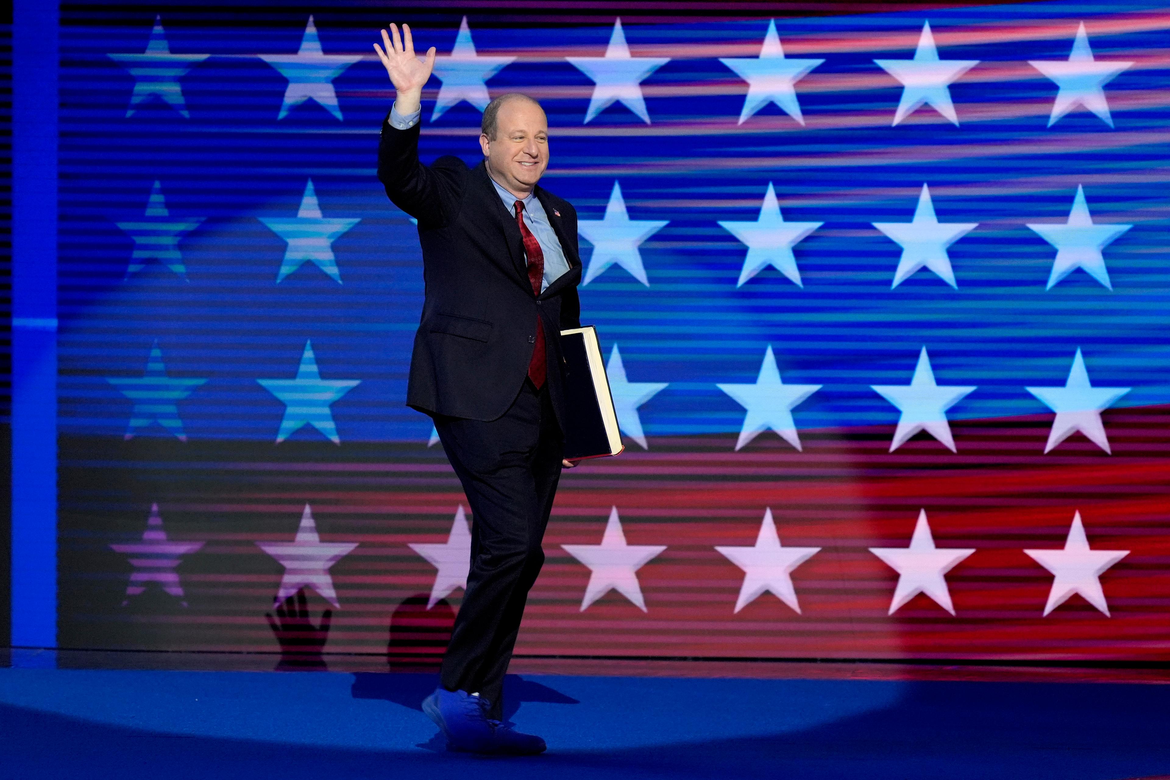 Colorado Gov. Jared Polis walking on stage at the Democratic National Convention, waving to the crowd.