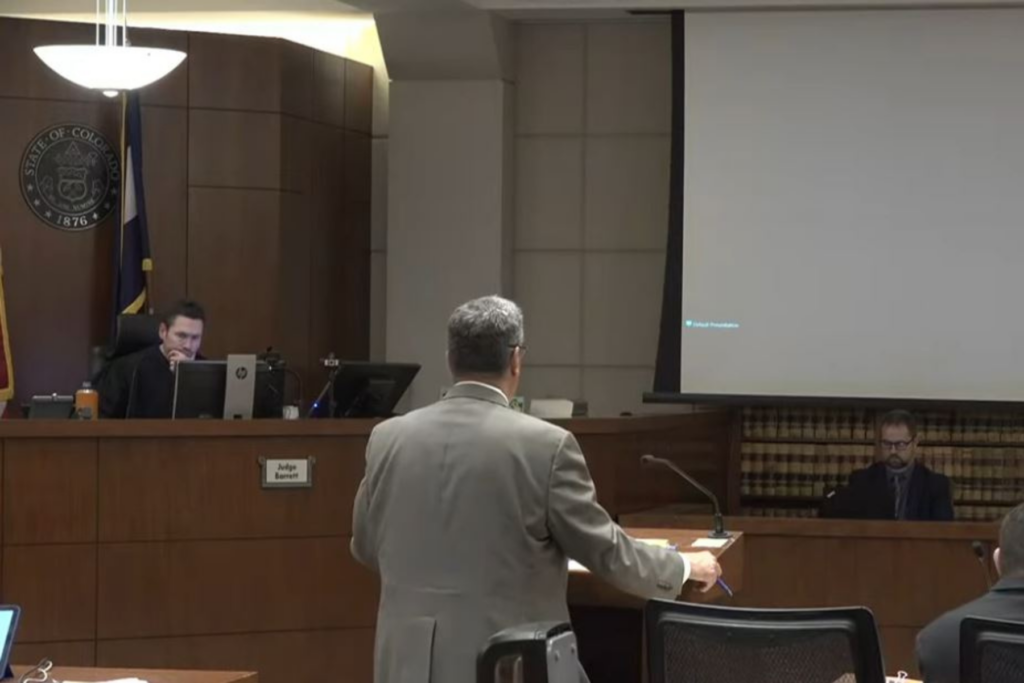 A judge in a black robe presides over a courtroom during cross-examination of a witness. Attorney Robert Shapiro, in a gray suit standing at a lectern, questions Sherronna Bishop, who is seated at a witness stand in white.