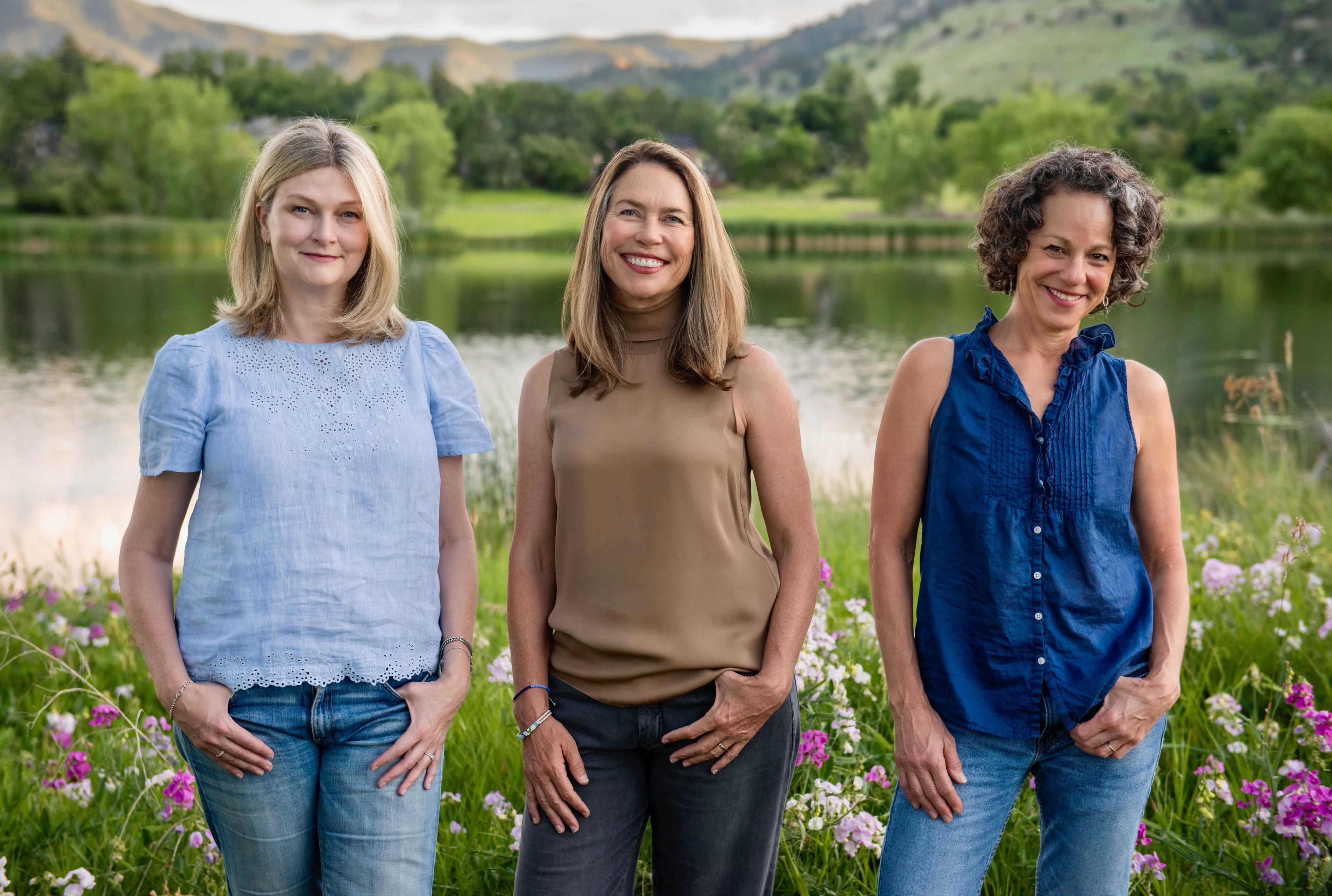 Angela Heisten, Annika Paradise, and Julie Frieder seen in front of a lake. They co-authored "Wonder Year: A Guide to Long-Term Family Travel and Worldschooling."