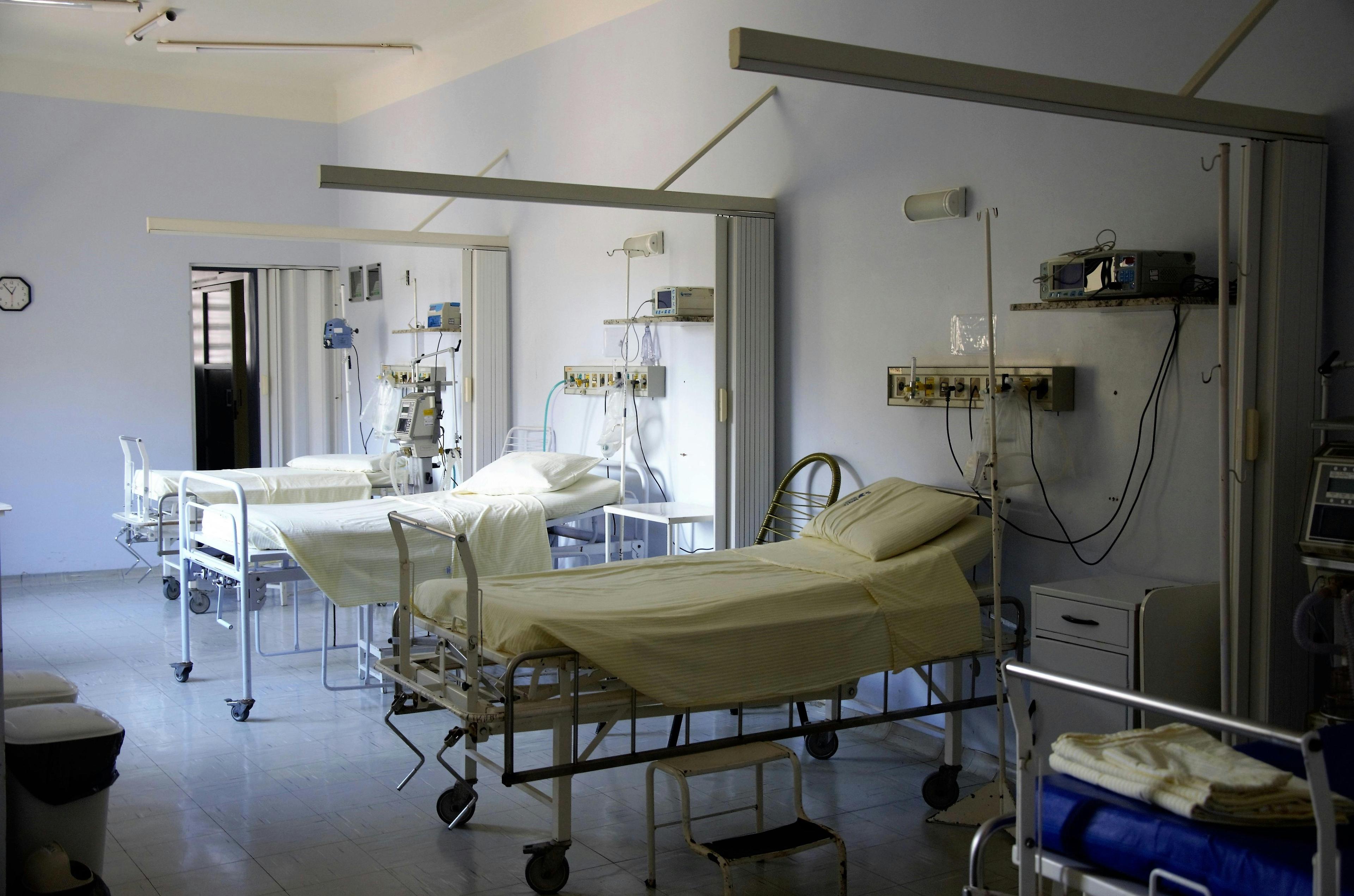 An empty hospital room with beds lined up and curtains pulled back.