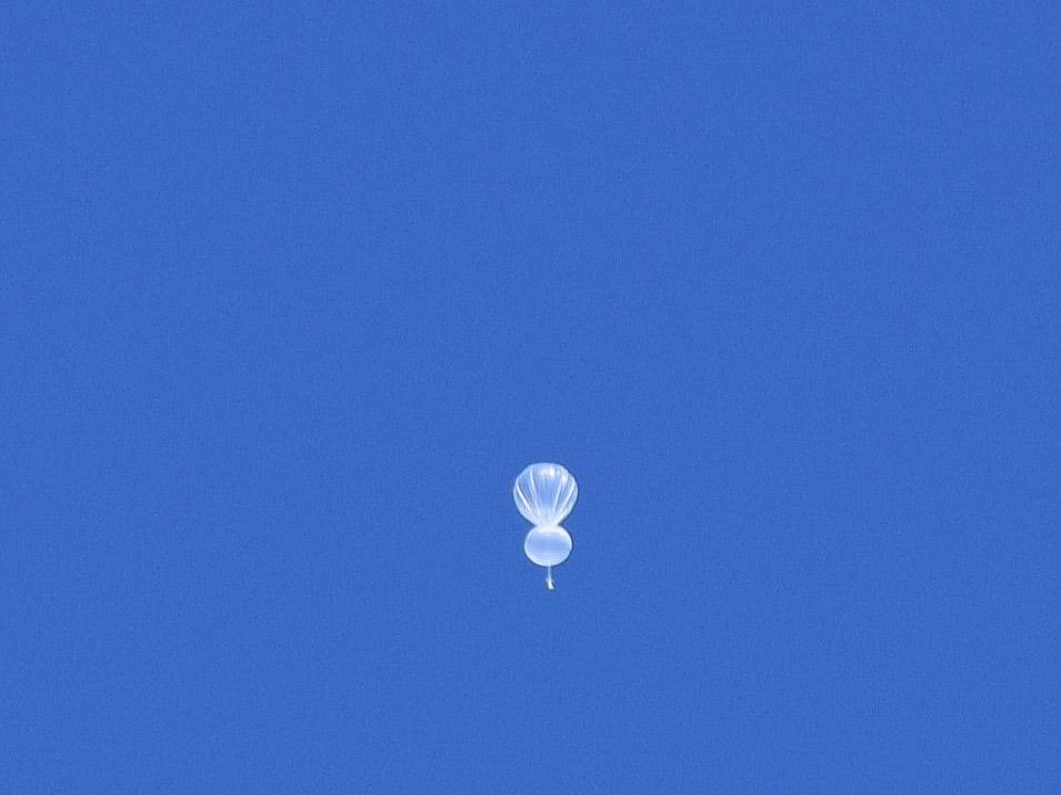 A white research balloon floating in a blue sky.