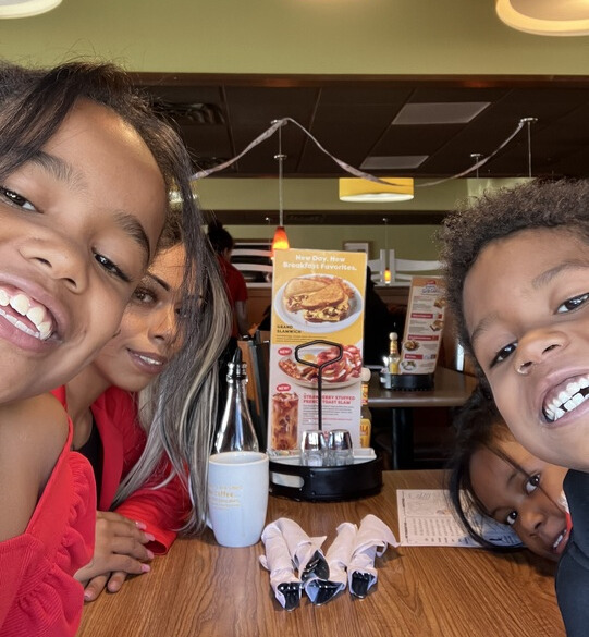 three kids and one adult leaning forward over table at pancake restaurant